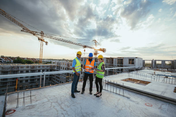 Three workers in safety vests and helmets standing in a warehouse