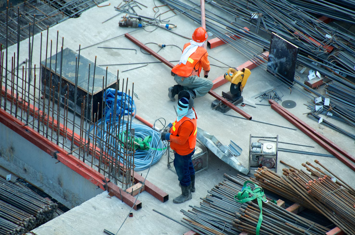 Two workers in orange safety vests and blue helmets standing in a field